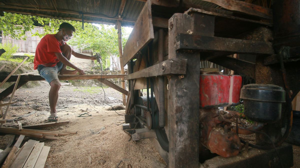 Tukang kayu di desa Mauliru sedang menyelesaikan pekerjaannya dengan mesin listrik dari genset
