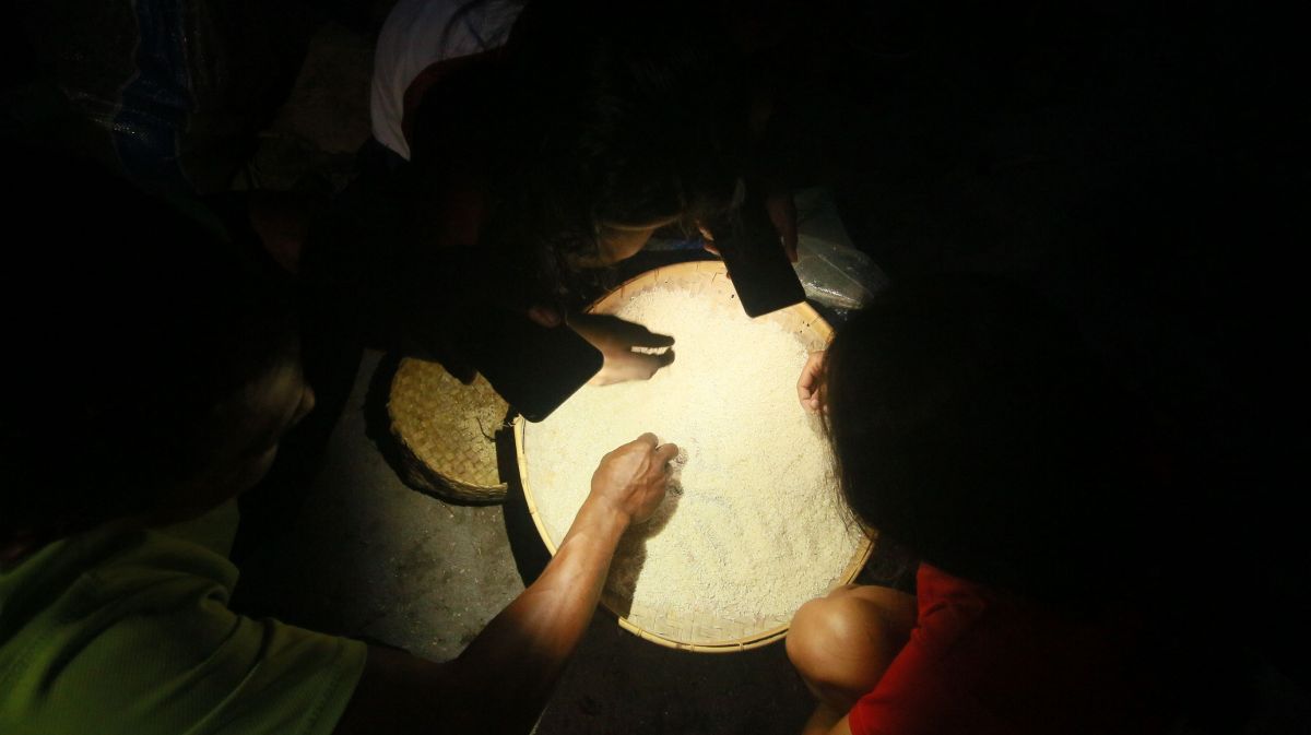 warga di Kampung Uwa, Pulau Palue sedang membersihkan beras dengan menggunakan lampu senter dari smartphone 