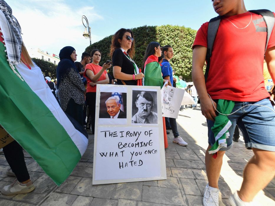 Seorang pengunjuk rasa berdiri dengan papan yang menunjukkan wajah Perdana Menteri Israel Benjamin Netanyahu dan pemimpin Nazi Jerman Adolf Hitler selama unjuk rasa solidaritas dengan warga Palestina di Aljazair pada 19 Oktober 2023. (AFP)