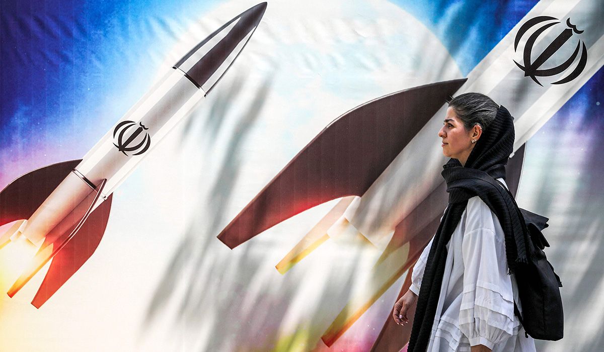Seorang wanita berjalan di depan banner bergambar rudal dengan emblem Iran.