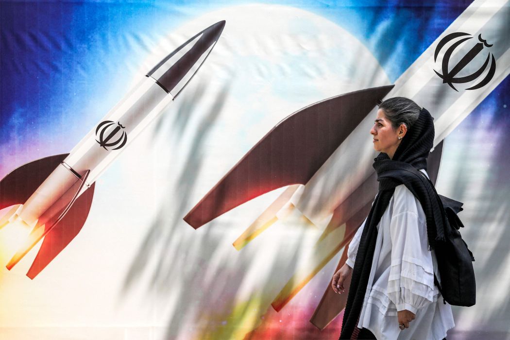 Ilustrasi: Seorang perempuan berjalan melewati spanduk yang menggambarkan peluncuran rudal Iran.